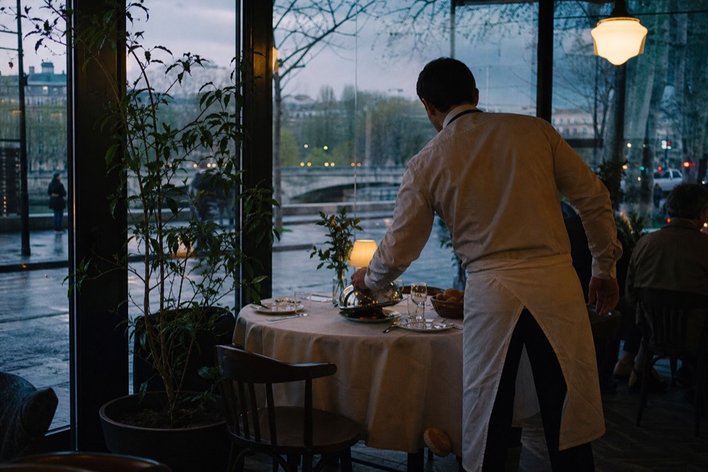 Waiter placing a covered plate on a dinner cruise table, no text, no logos, no people