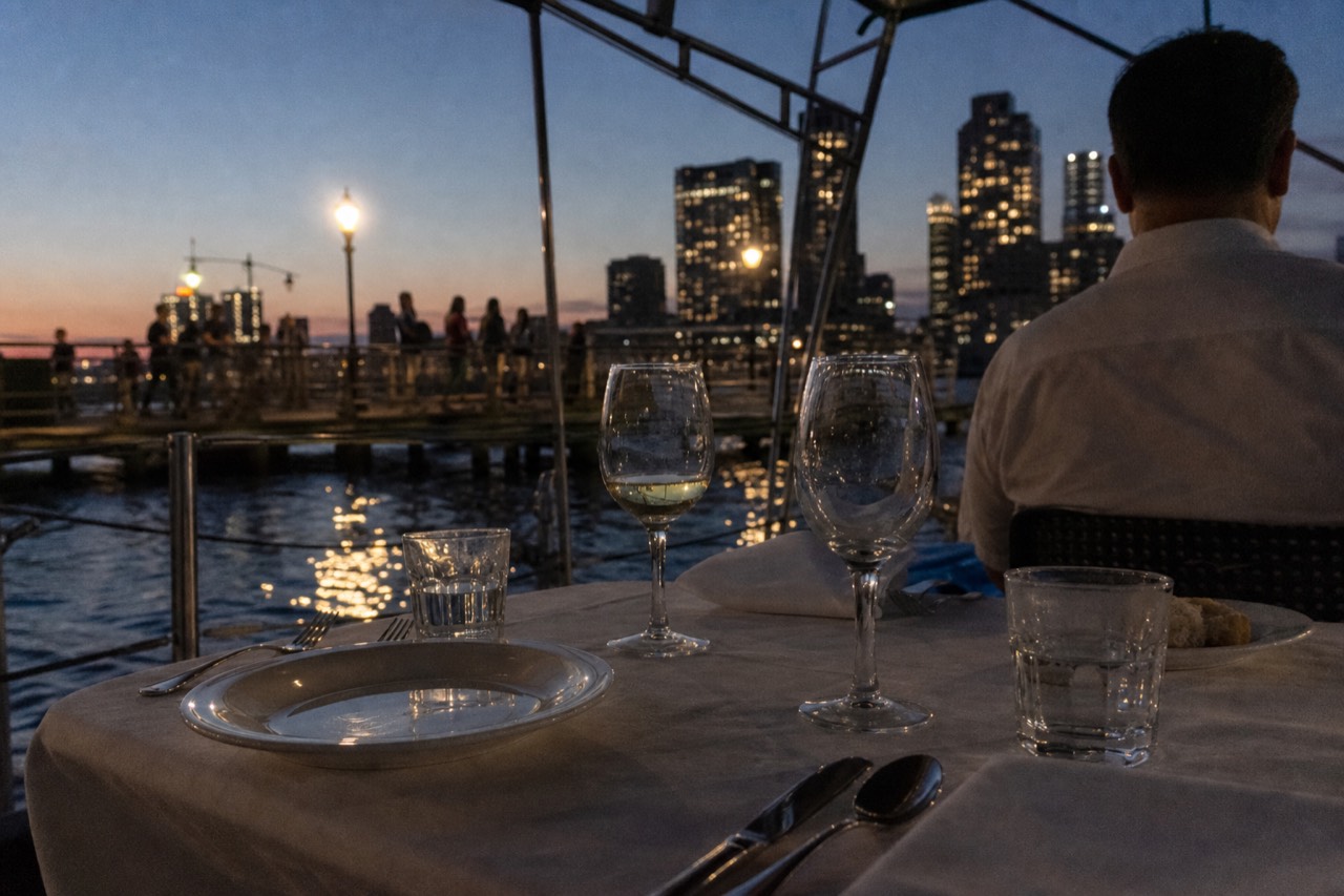 Set dinner table with wine glasses aboard a Seine cruise boat at dusk, no text, no logos, no people