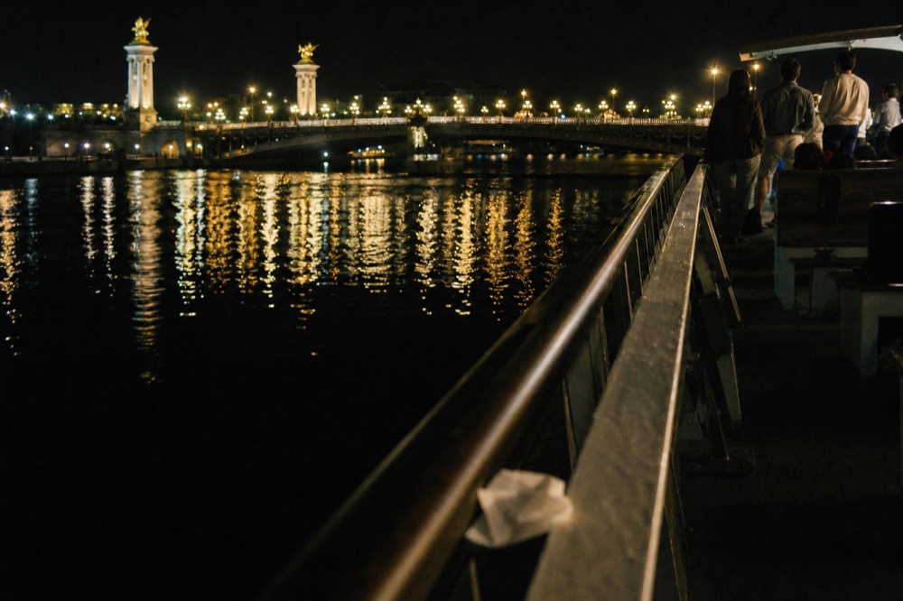 Night view of the Seine from a cruise deck with the illuminated Pont Alexandre III in the background, no text, no logos, no people.