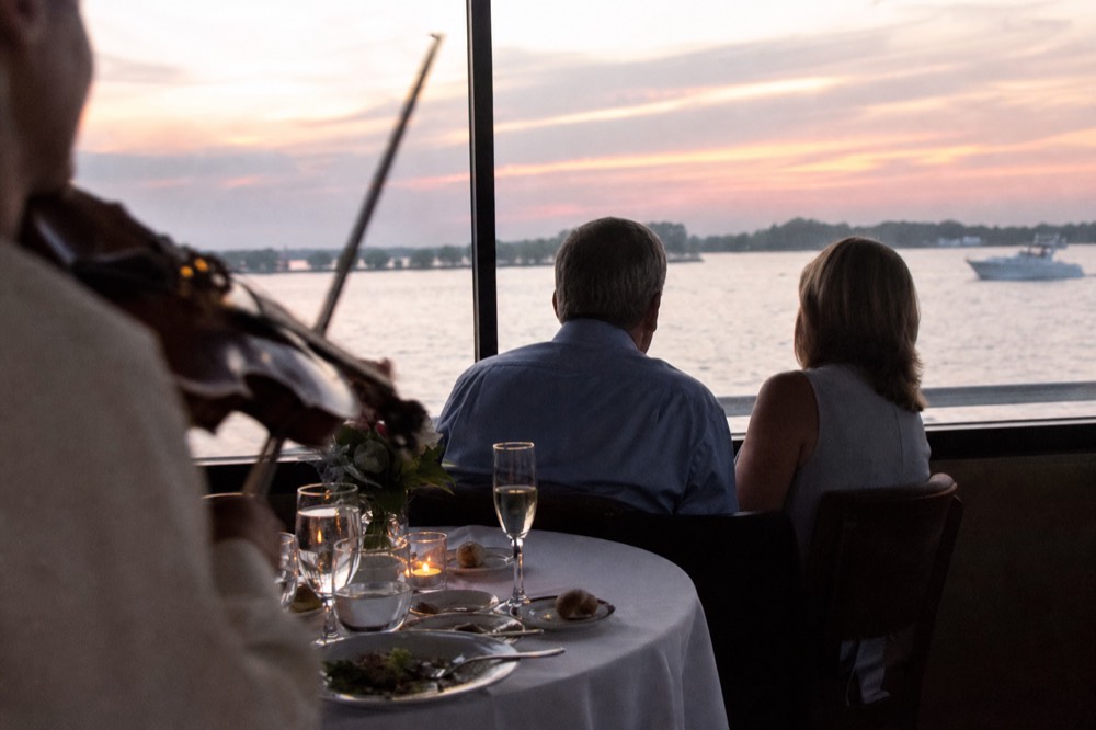 Dinner table on a Bateaux Mouches boat with a violinist performing near the window, no text, no logos, no people
