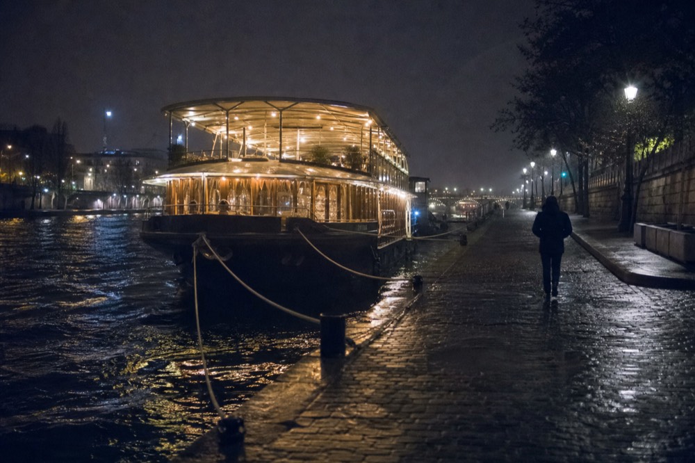 Dinner cruise boat lit at night moored on the Seine with city lights reflecting on water, no text, no logos, no people