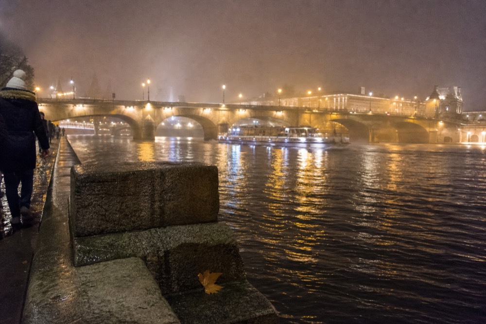 Wide view of the Seine at night with illuminated bridges and a cruise boat passing, no text, no logos, no people