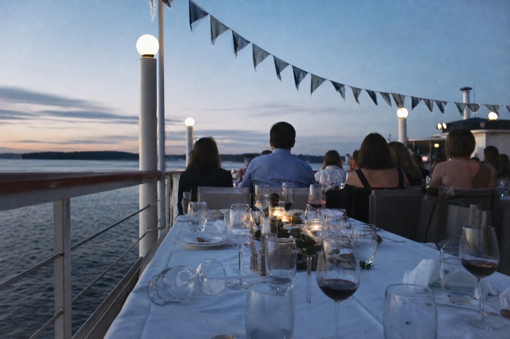 A long dinner table set with wine glasses on a casually lit Seine cruise deck, no text, no logos, no people.
