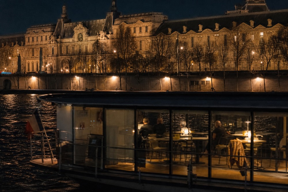 Passenger dinner boat passing illuminated Parisian architecture at night, no text, no logos, no people