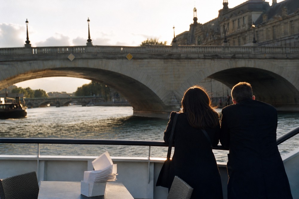Open upper deck of a Seine cruise boat passing stone bridges at golden hour, no text, no logos, no people