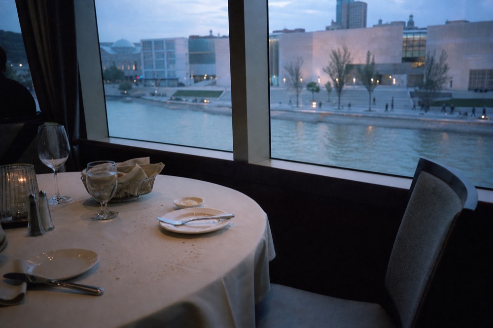 Set dinner table beside a window on a Seine cruise boat with city lights beyond, no text, no logos, no people