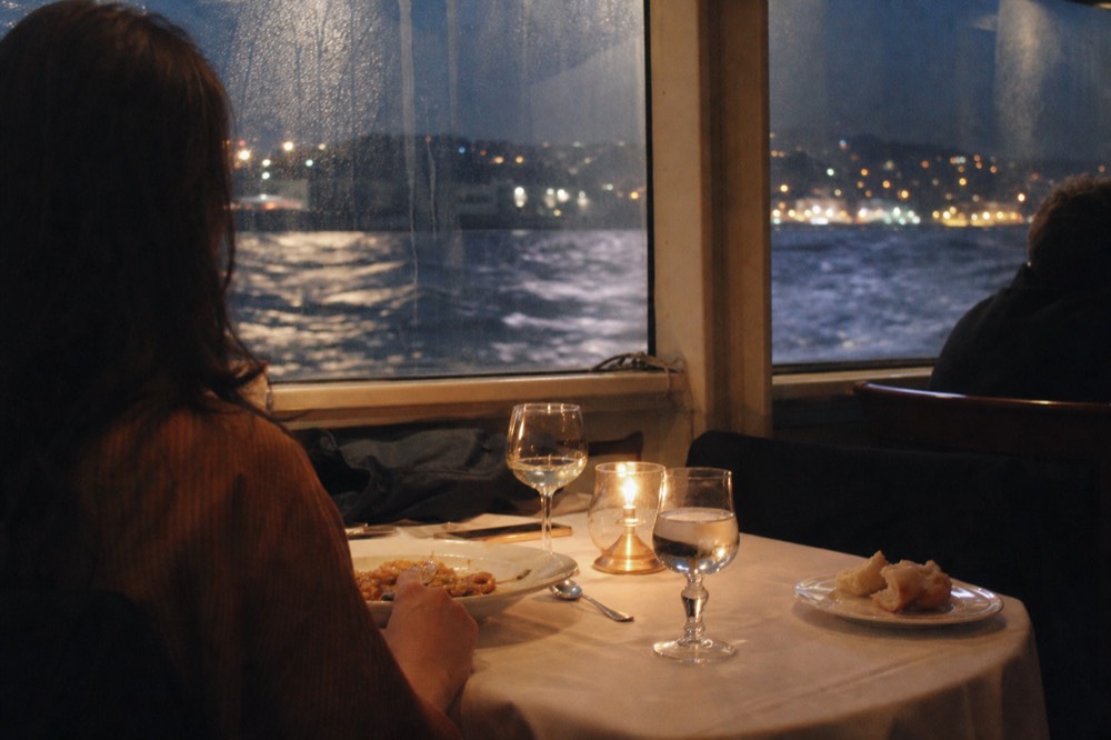 Candlelit dinner table set on a Seine cruise boat with Paris lights outside the window, no text, no logos, no people