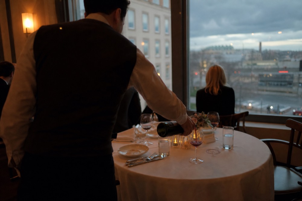 Waiter pouring wine at a set dinner table aboard a Seine cruise boat, no text, no logos, no people