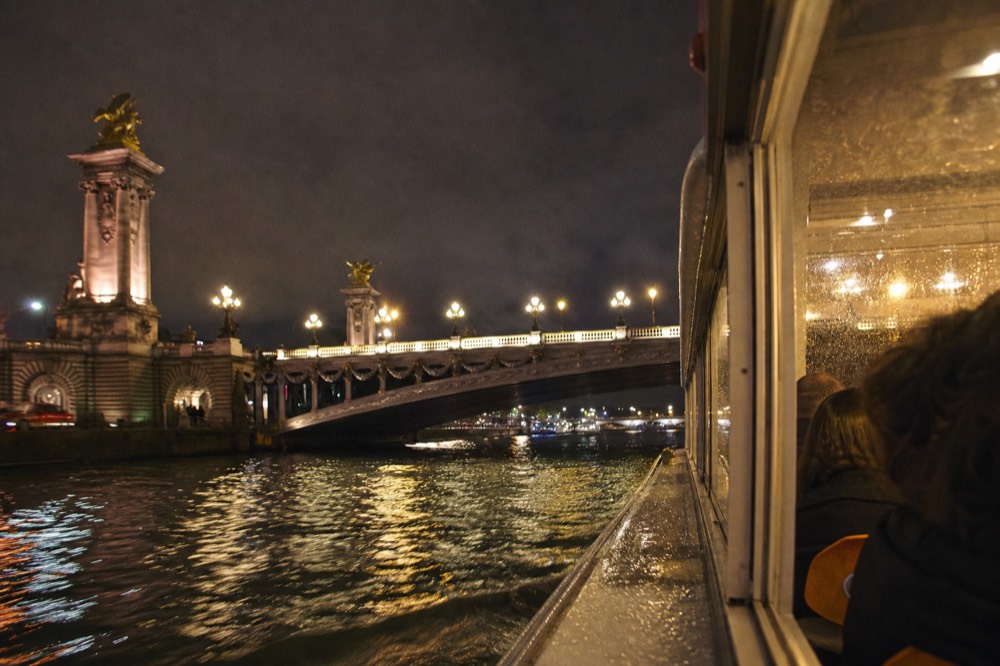 Dinner cruise boat passing lit bridges on the Seine at night, no text, no logos, no people