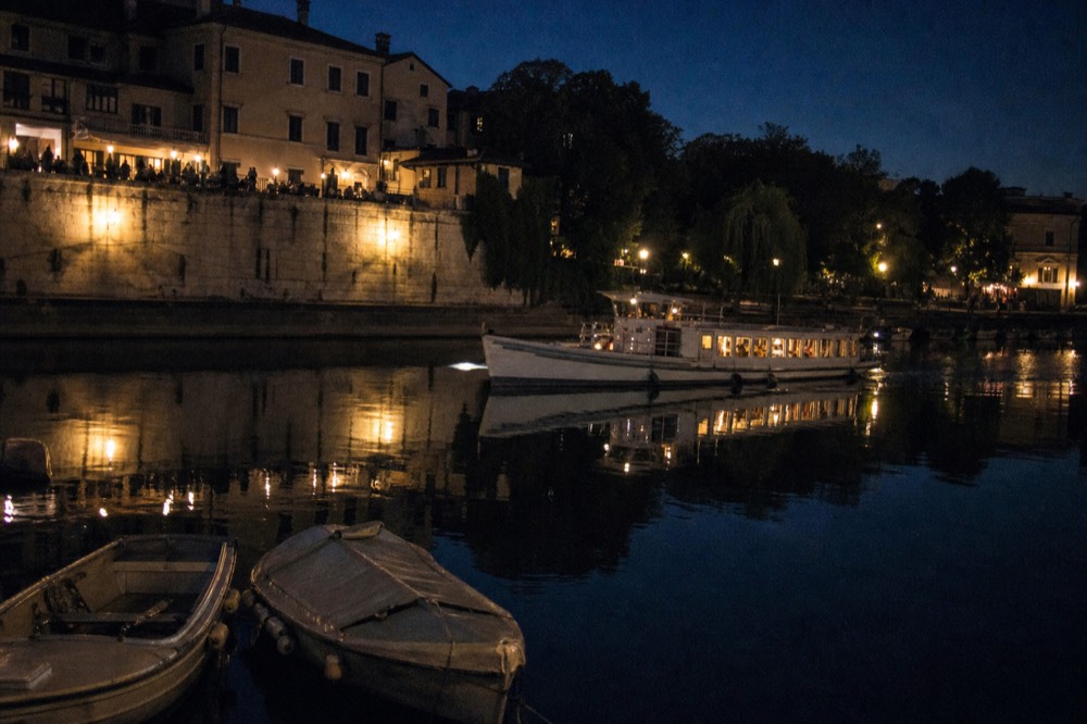 Night view of an illuminated Paris dinner cruise boat passing a lit bridge, no text, no logos, no people