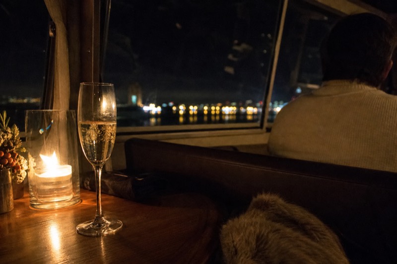 A Champagne glass on a candlelit table aboard a Seine dinner boat at night
