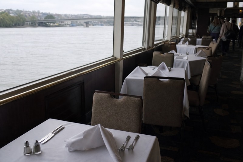 Dinner tables set by the windows of a glass-enclosed Seine dinner boat