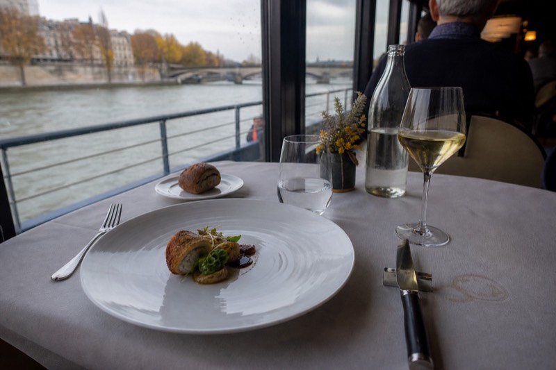 A plated gourmet dinner course on a Seine dinner cruise with the river outside the window