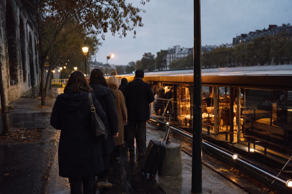 A dinner boat moored at a lit Paris quay in the evening with passengers waiting to board, no text, no logos, no people