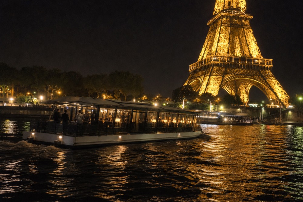A modern electric dinner boat passing the illuminated Eiffel Tower on the Seine at night, no text, no logos, no people