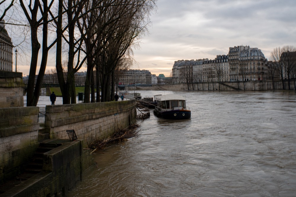 A high-water Seine with a moored cruise boat and Paris bridges in evening light, no text, no logos, no people