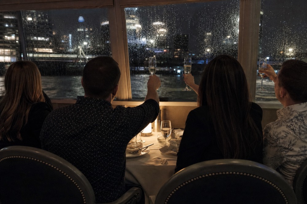 Couples and small groups toasting with champagne glasses at a dinner cruise table beside a window, no text, no logos, no people