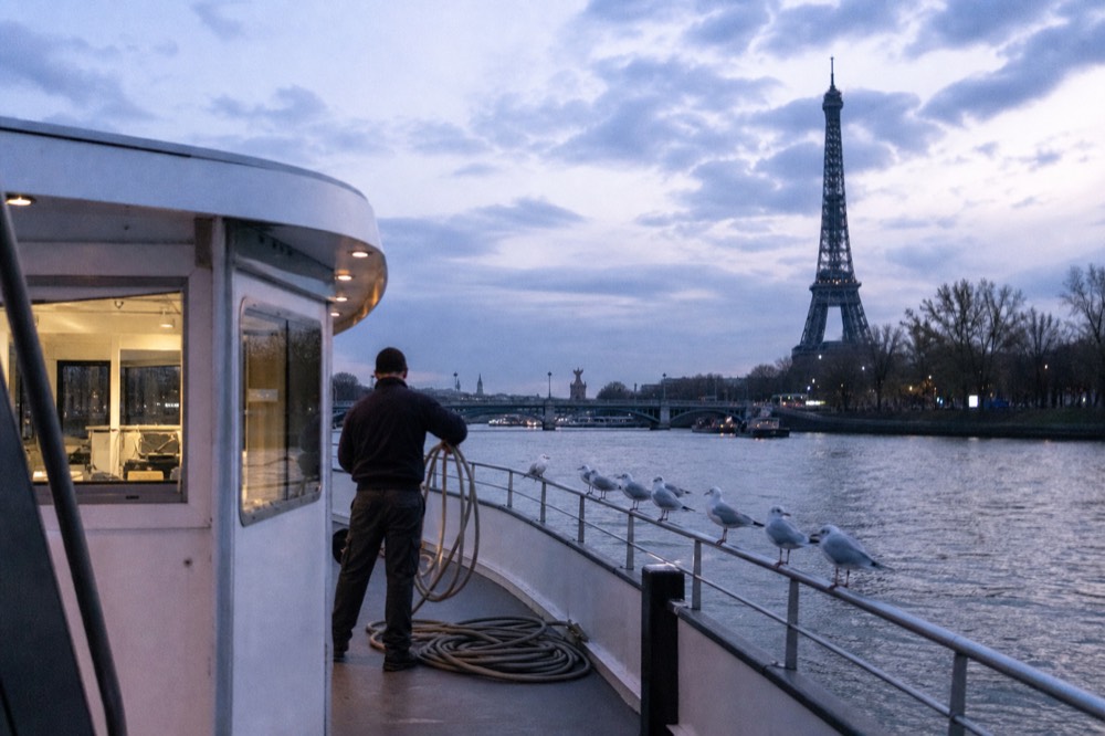 The exterior of a passenger boat moored on the Seine at dusk near the Eiffel Tower, no text, no logos, no people