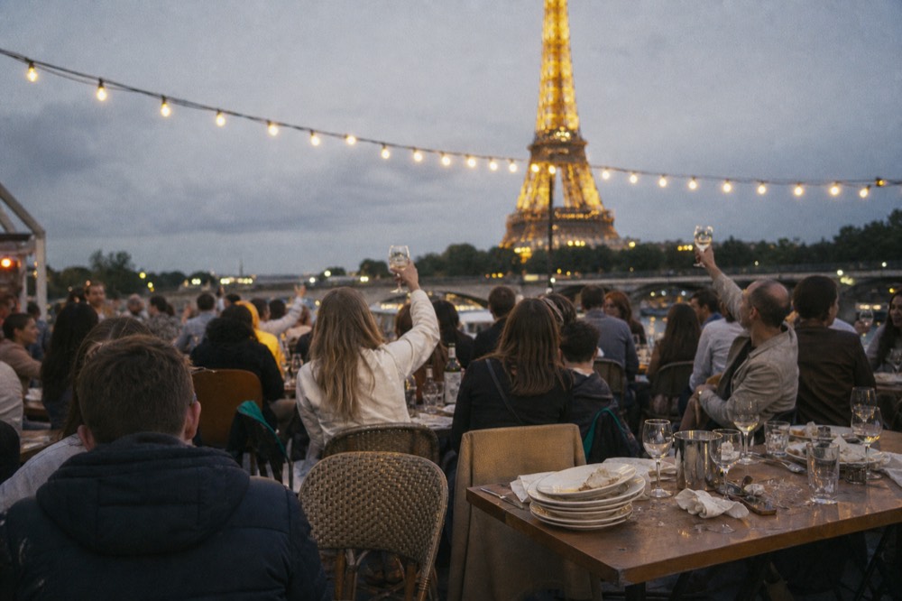 A dinner cruise boat lit up at night with a crowded open deck and city lights behind, no text, no logos, no people