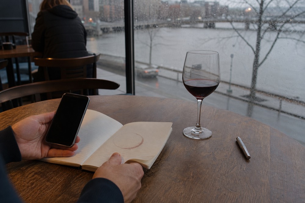 A notebook and phone showing cruise research beside a glass of wine on a wooden table, no text, no logos, no people