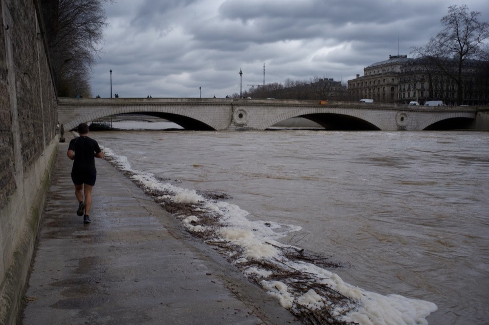 A high, fast-flowing Seine under dark clouds with a bridge in the background, no text, no logos, no people