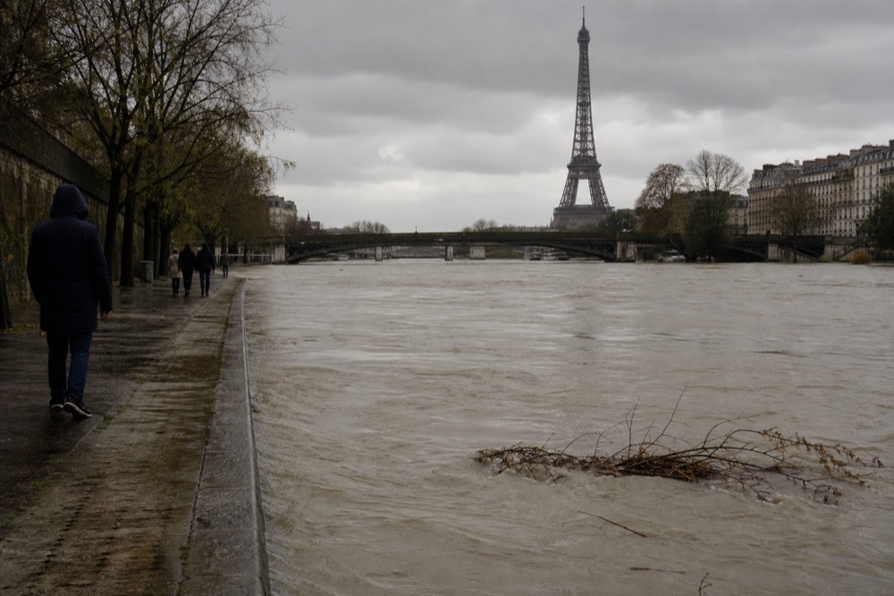 Eiffel Tower and Seine quay with river surface touched by flood debris, no text, no logos, no people