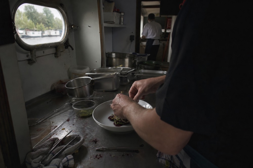A chef plating a gourmet course in a river boat's galley kitchen, no text, no logos, no people.