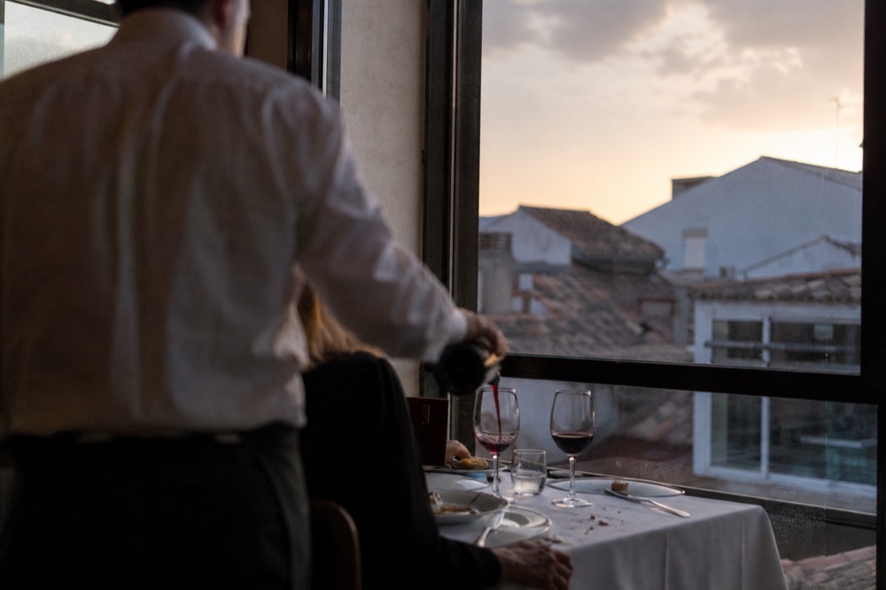 A waiter pouring wine at a dinner cruise table with the Paris skyline behind, no text, no logos, no people.