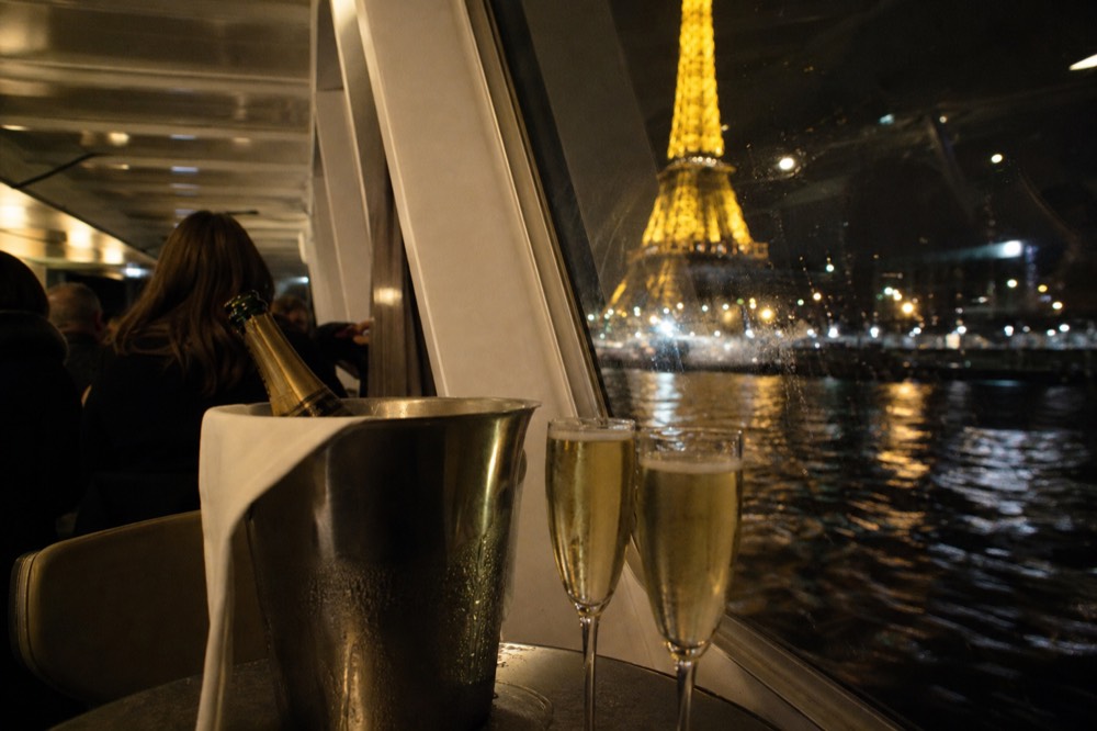 A Champagne bucket and two flutes on a table with the illuminated Eiffel Tower in the background, no text, no logos, no people