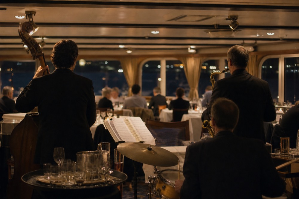 A jazz quartet performing on a Seine dinner cruise with diners at white-tablecloth tables, no text, no logos, no people