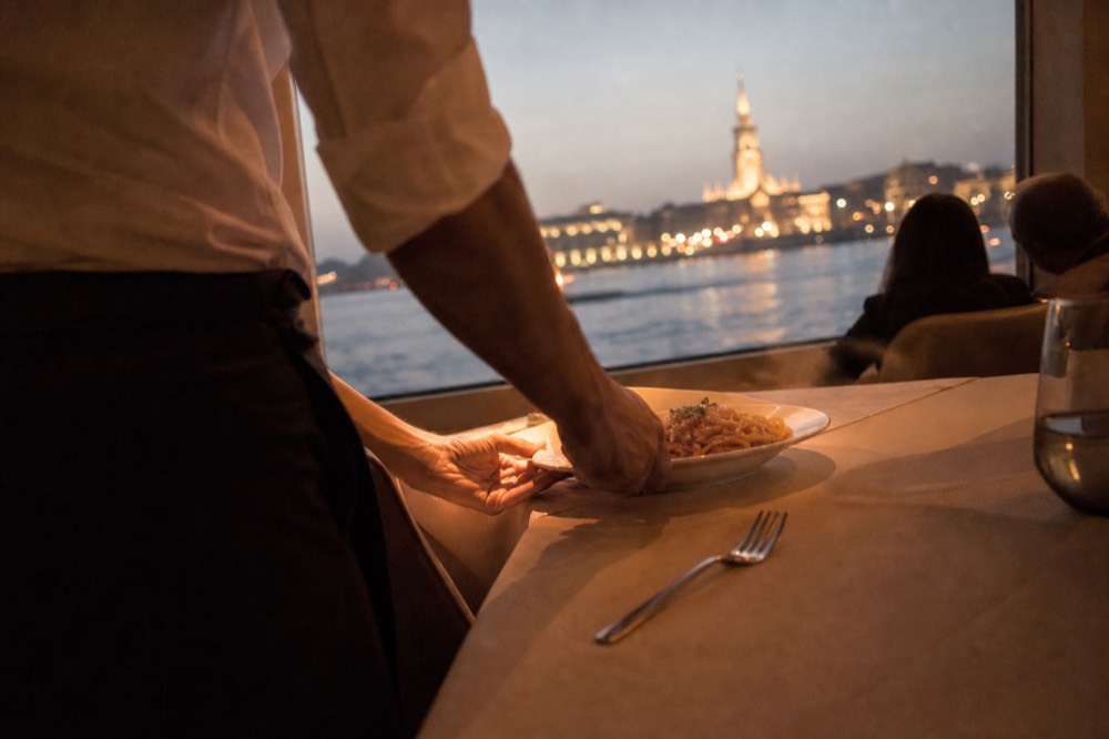 An Italian pasta dish being served on a Seine dinner cruise with the Eiffel Tower visible through the window, no text, no logos, no people